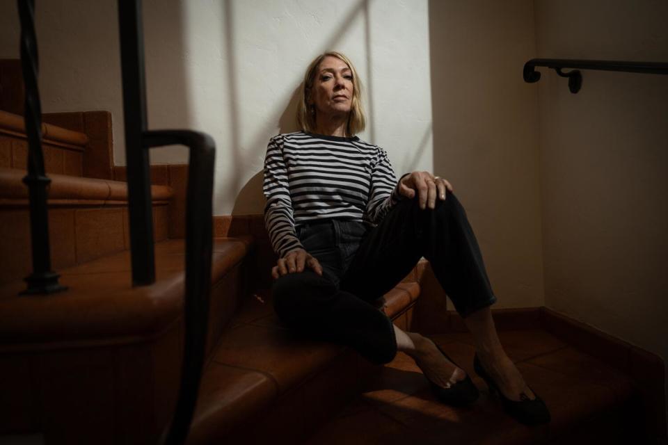 Woman in black and white stripped shirt sits on a set of stairs inside her house,