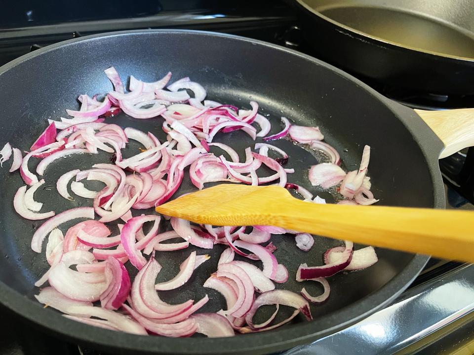 red onion slices cooking in a black pan with a wooden spoon