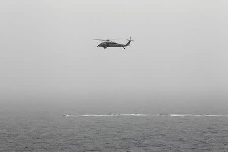 Three Iranian Revolutionary Guard boats are seen near the U.S. aircraft carrier, USS George H. W. Bush while transiting Straits of Hormuz as U.S. Navy helicopter hovers over them during early hours of March 21, 2017. Picture taken March 21, 2017. REUTERS/Hamad I Mohammed