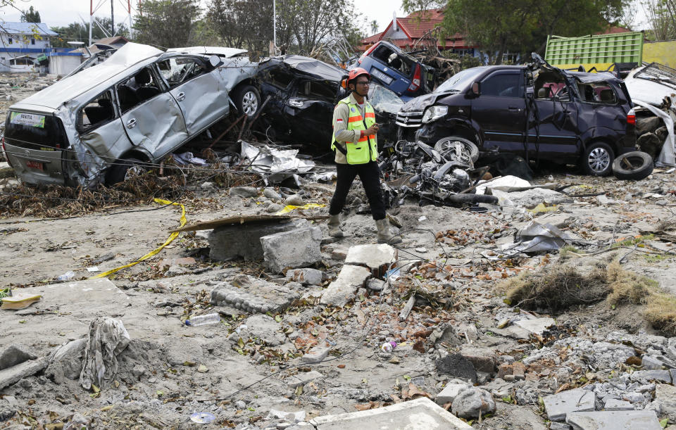 A man walks past remains of cars that were destroyed in the massive earthquake and tsunami that hit Palu, Central Sulawesi, Indonesia Thursday, Oct. 4, 2018. Life is on hold for thousands living in tents and shelters in the Indonesian city hit by a powerful earthquake and tsunami, unsure when they'll be able to rebuild and spending hours each day often futilely trying to secure necessities such as fuel for generators. (AP Photo/Aaron Favila)