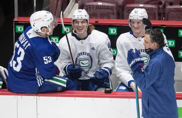 Adam Gaudette laughs while on the bench with Bo Horvat, left, and Tyler Myers, as head coach Travis Green skates past. Gaudette was the first Canucks player to test positive for COVID-19 on March 30.  (Darryl Dyck/The Canadian Press - image credit)