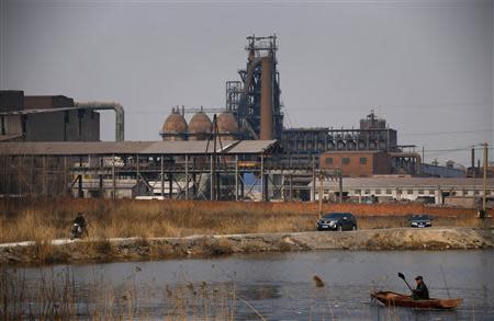 A man uses a shovel to break the ice on the frozen waters of a fish farm near an abandoned steel mill (background) of Qingquan Steel Group in Qianying township, Hebei province February 18, 2014. REUTERS/Petar Kujundzic