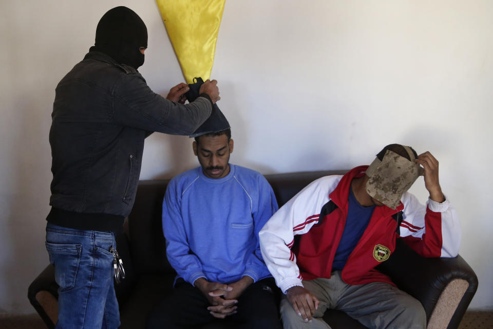 FILE - In this March 30, 2018, file, photo, a Kurdish security officer takes off face masks from Alexanda Amon Kotey, left, and El Shafee Elsheikh, who were allegedly among four British jihadis who made up a brutal Islamic State cell dubbed "The Beatles," for an interview at a security center in Kobani, Syria. The Islamic State group could get a new injection of life if conflict erupts between the Kurds and Turkey in northeast Syria as the U.S. pulls its troops back from the area. The White House has said Turkey will take over responsibility for the thousands of IS fighters captured during the long campaign that defeated the militants in Syria. But it’s not clear how that could happen. (AP Photo/Hussein Malla, File)