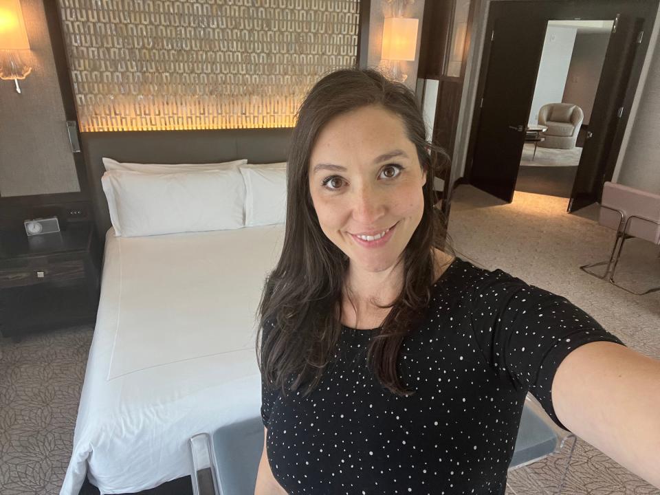A woman taking a selfie in front of a hotel bed.