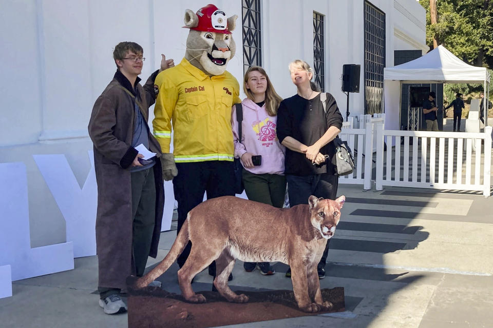 People pose for pictures next to a cardboard cutout of Hollywood's most famous mountain lion, P-22, during his public memorial put on by the "Save LA Cougars," at the Greek Theater in Griffith Park in Los Angeles Saturday, Feb. 4, 2023. (AP Photo/Stefanie Dazio)