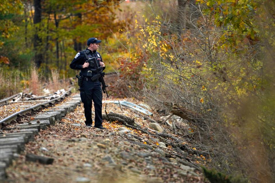 A police officer searches along railroad tracks near the Androscoggin River for the suspect in this week's deadly mass shootings, Friday, Oct. 27, 2023, in Lisbon, Maine. The manhunt continues for the man who killed at least 18 in separate shootings at a bowling alley and restaurant in Lewiston on Wednesday.