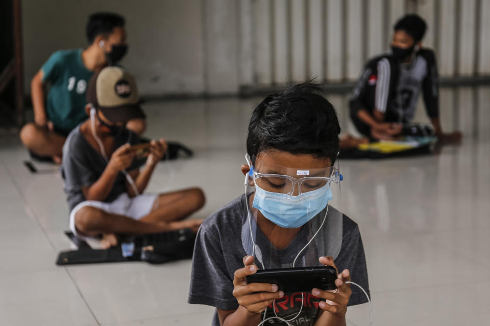 Students use smartphones to work on online school assignments using free internet network while practicing physical distancing at a public hall in Ubung Kaja Village, Denpasar, Bali, Indonesia on July 21, 2020. (Photo by Johanes Christo/NurPhoto via Getty Images)