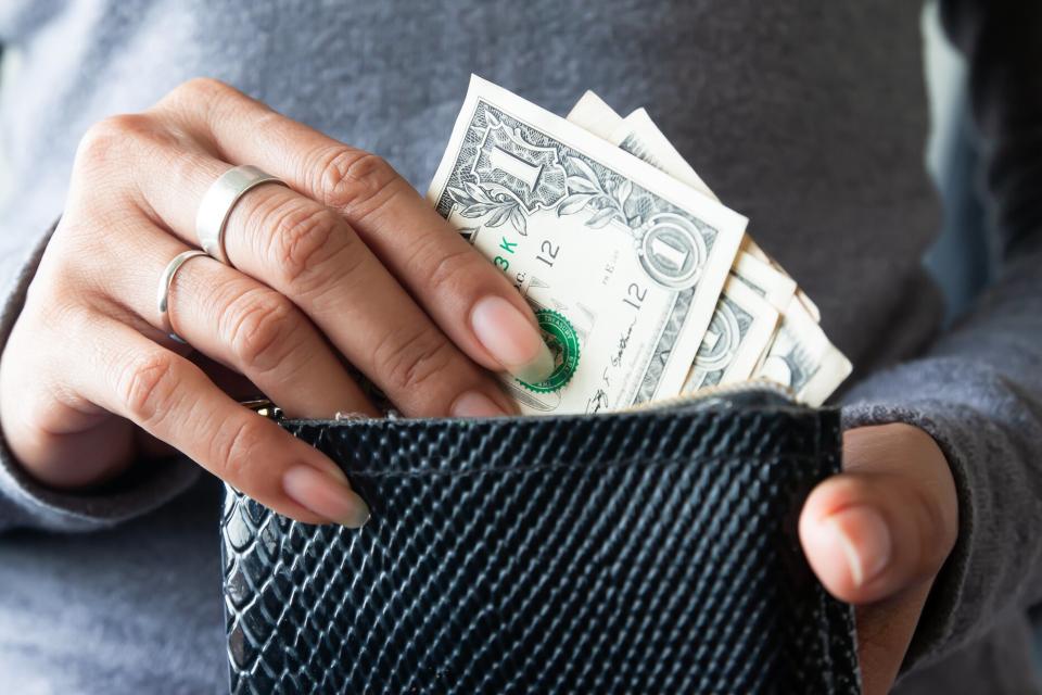 woman extracting one dollar bills from black wallet