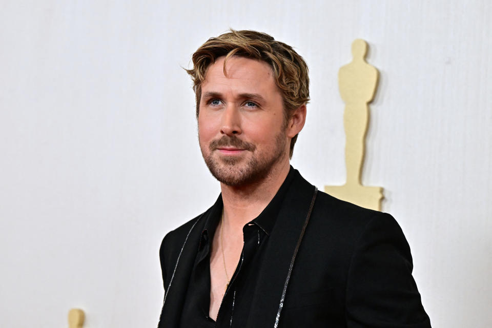 Ryan in a dark suit jacket and shirt posing at an event; Oscars statuette visible in the background