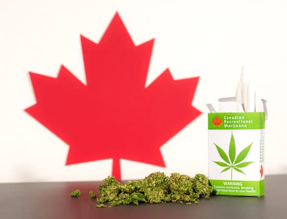 Canadian maple leaf cutout next to marijuana buds and pack of marijuana cigarettes.