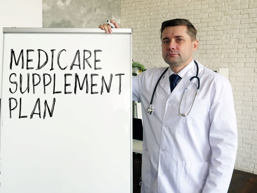 A doctor stands next to a dry erase board with Medicare Supplement Plan written on it