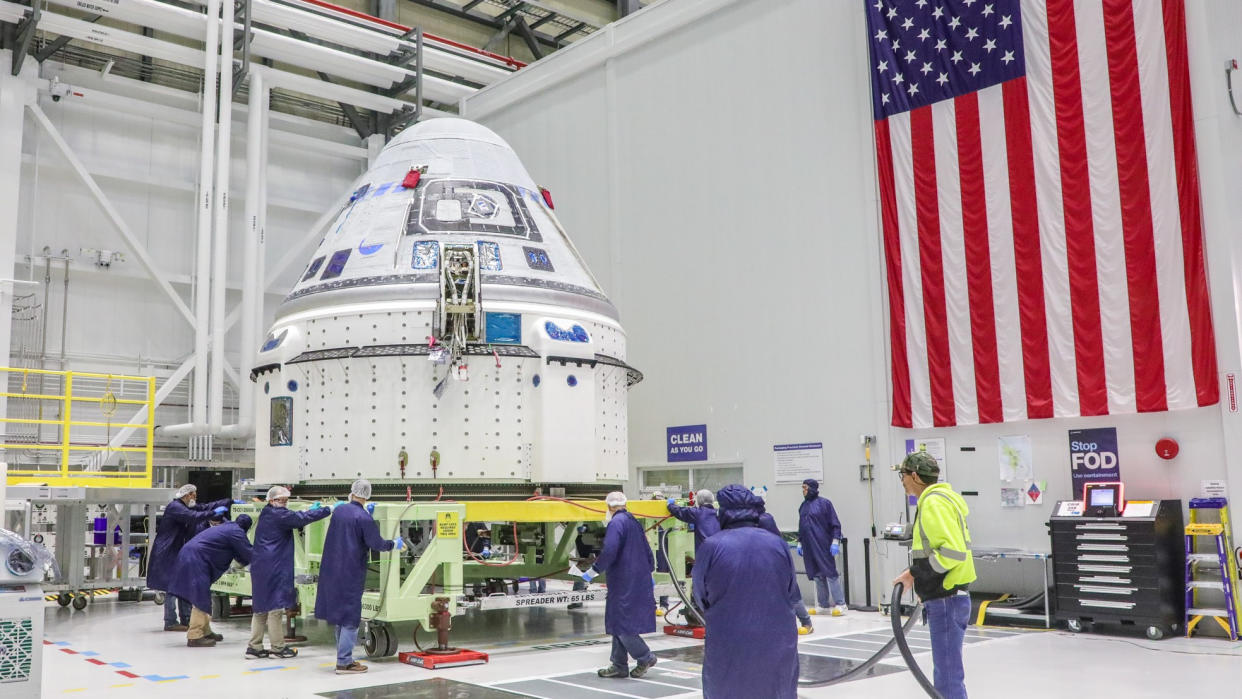  People in blue lab coats working on Boeing's blue and white Starliner spacecraft 