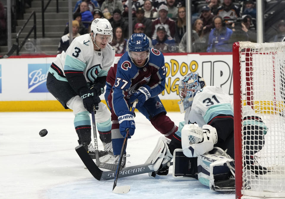 Colorado Avalanche left wing J.T. Compher, center, has his shot blocked by Seattle Kraken goaltender Philipp Grubauer, right, after driving past Kraken defenseman Will Borgen in the first period of an NHL hockey game Sunday, March 5, 2023, in Denver. (AP Photo/David Zalubowski)
