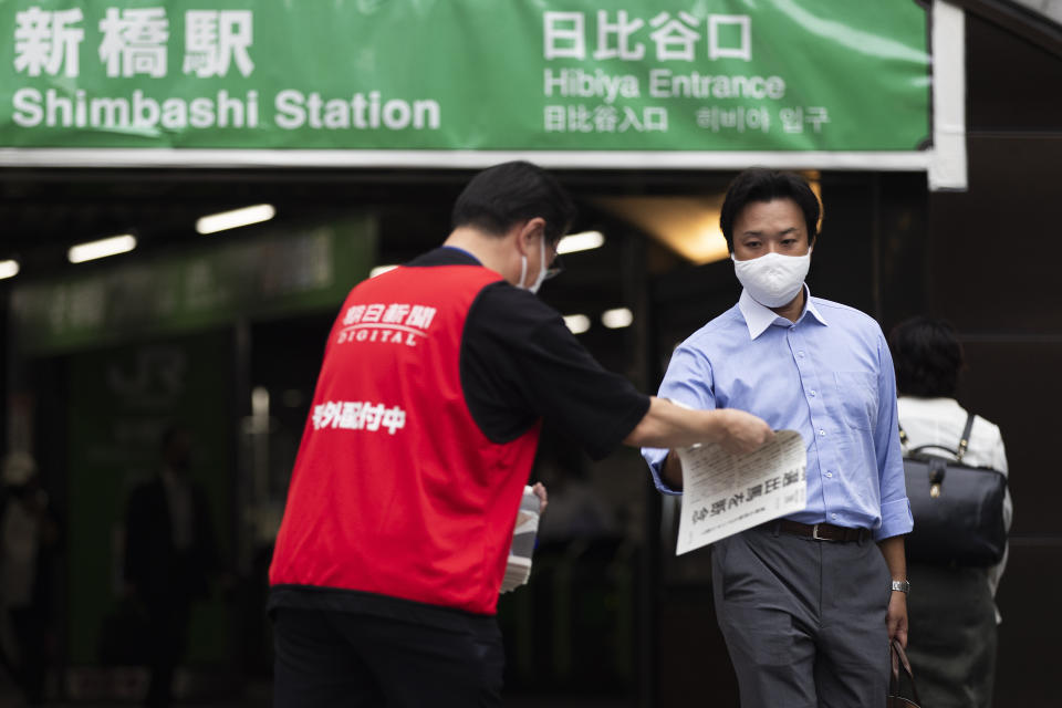 A staffer, left, for a Japanese newspaper hands out a copy of the extra issue for Japanese Prime Minister Yoshihide Suga's announcement of not running for leadership of the governing party later this month, near a train station in Tokyo, Friday, Sept. 3, 2021. Suga said Friday he won't run for leadership of the governing party at the end of this month, paving the way for a new Japanese leader after just a year in office. (AP Photo/Hiro Komae)