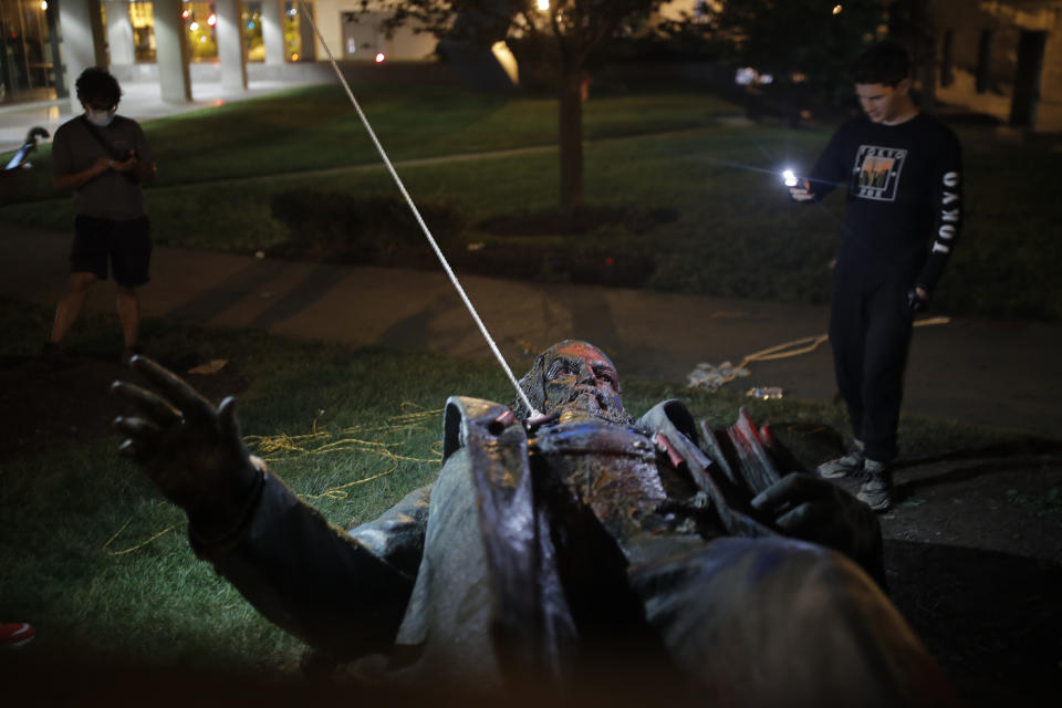 Un hombre usa su celular para grabar la estatua de Albert Pike, la única de un general del ejército confederado en la capital de Estados Unidos, después de que fue derribada por manifestantes e incendiada en Washington en las primeras horas del sábado 20 de junio de 2020. (AP Foto/Maya Alleruzzo)