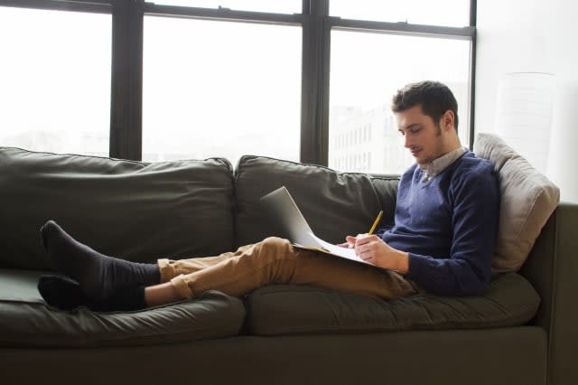 Young Man Relaxing on Couch and Doing Homework