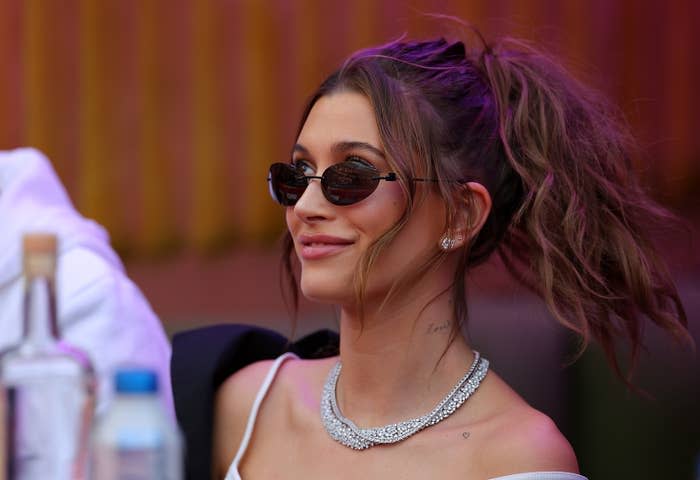 Hailey smiling as she looks up. She's wearing sunglasses and a diamond necklace