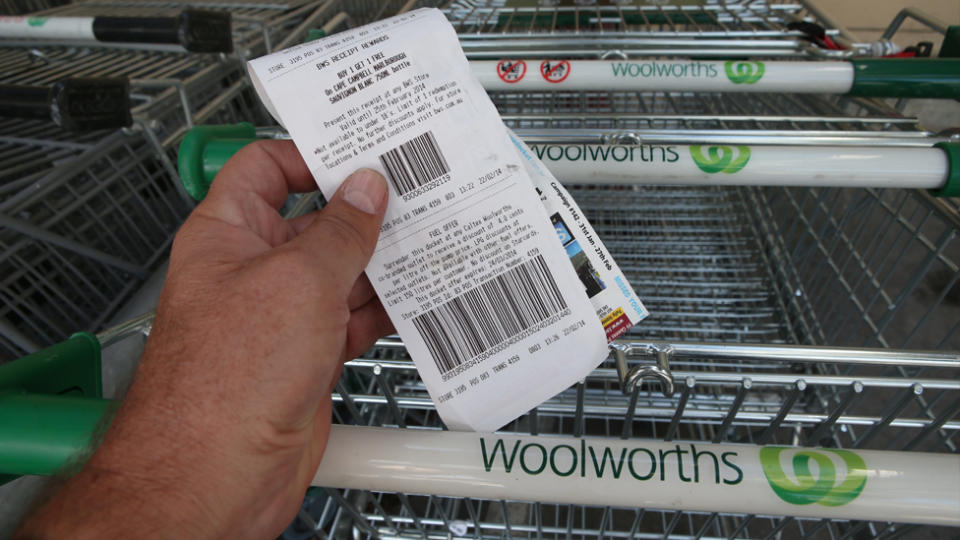 A Woolworths shopper holds a receipt in front of Woolworths trollies. 