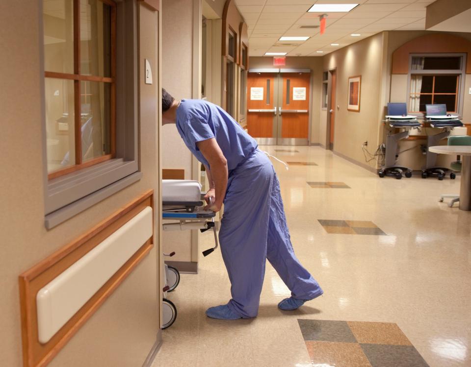 A healthcare worker rolls a patient gurney into a patient room.