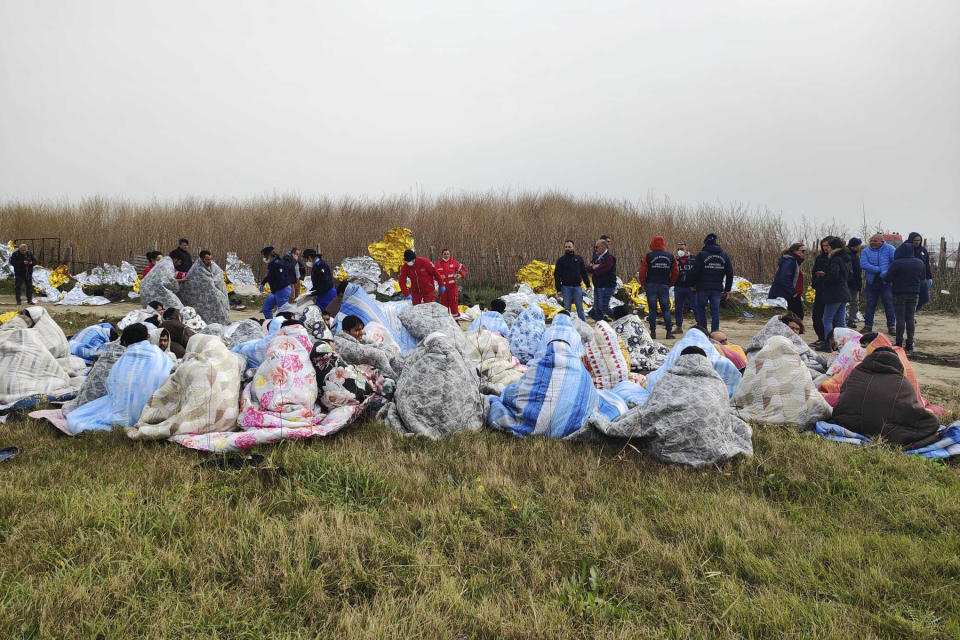 Rescued migrants sit covered in blankets at a beach near Cutro, southern Italy, Sunday, Feb. 26, 2023. Nearly 70 people died in last week's shipwreck on Italy's Calabrian coast. The tragedy highlighted a lesser-known migration route from Turkey to Italy for which smugglers charge around 8,000 euros per person. (Antonino Durso/LaPresse via AP, File)