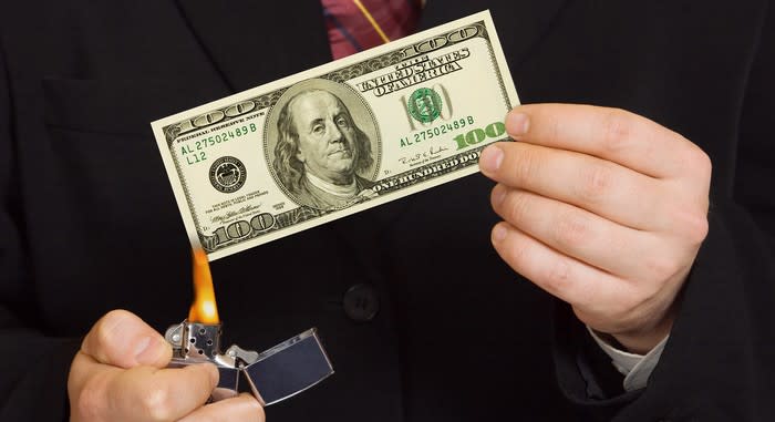 A person holding a one hundred dollar bill and setting it on fire with a lighter.