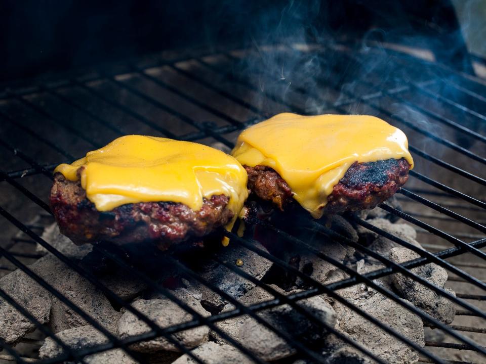 Two hamburgers with melted cheese on a smoking charcoal grill.