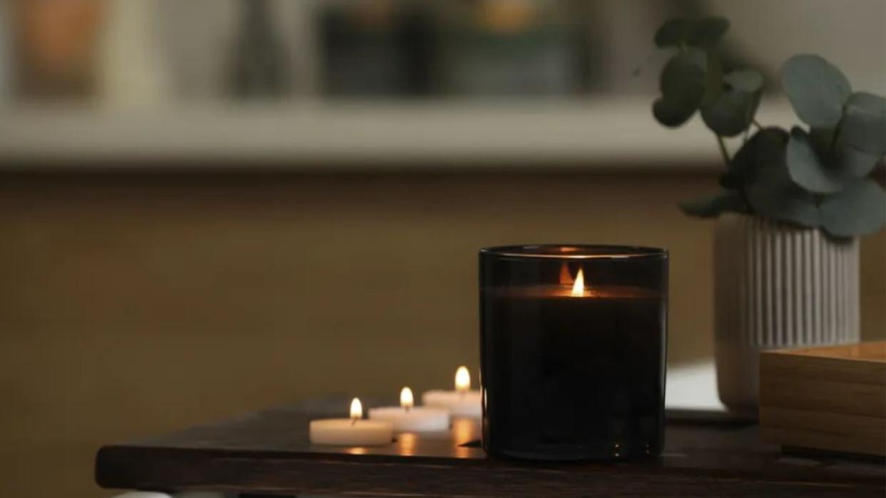  Lit scented candle in black glass vessel in room. 