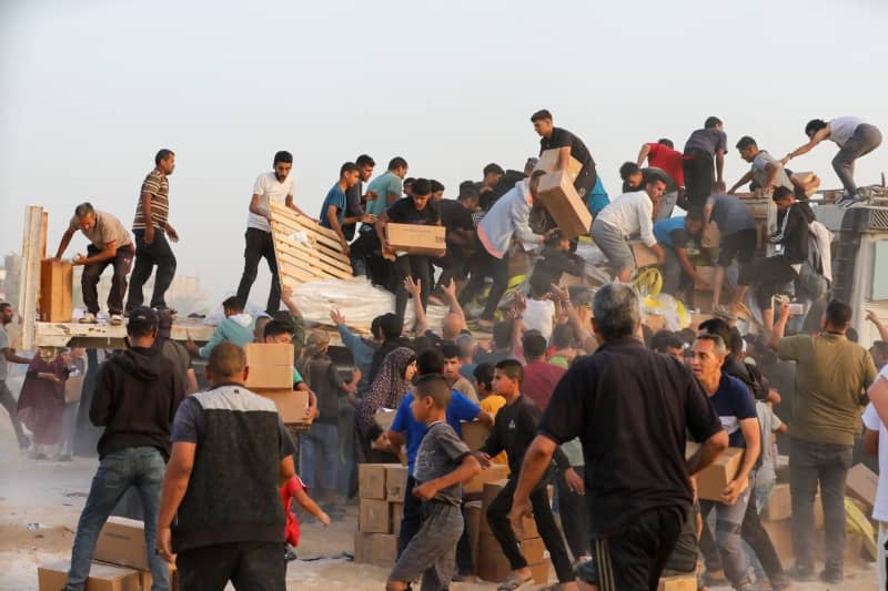Palestinians carry boxes of humanitarian aid after rushing the trucks transporting the international aid from the US-built Trident Pier near Nuseirat. Ali Hamad/APA Images via ZUMA Press Wire/dpa