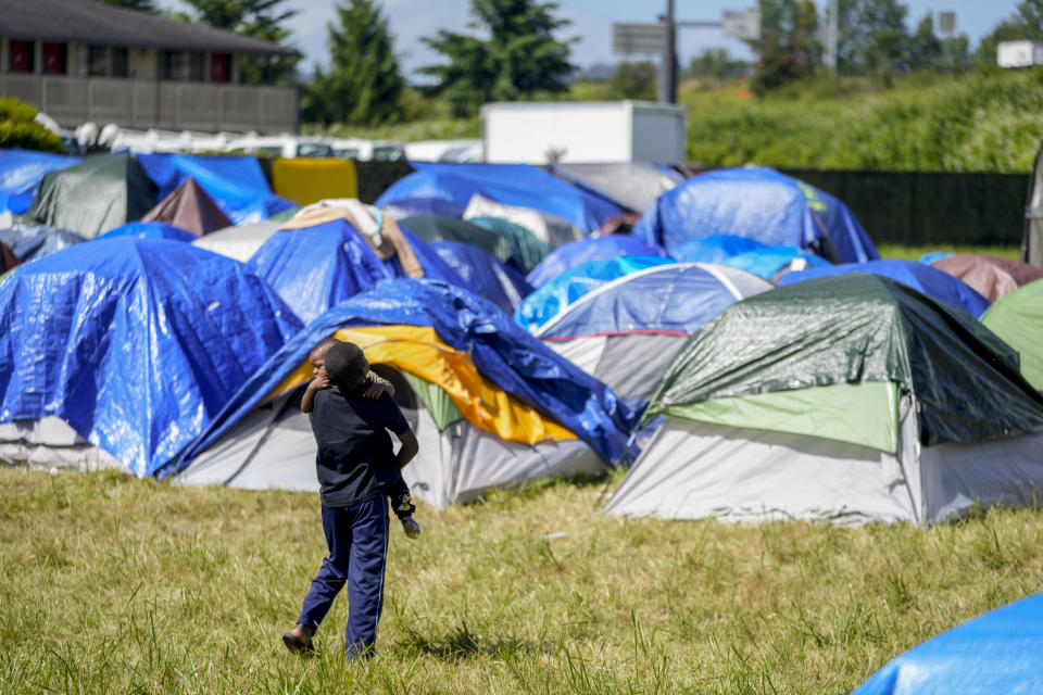 A child carries another through an encampment of asylum-seekers mostly from Venezuela, Congo and Angola next to an unused motel owned by the county, Wednesday, June 5, 2024, in Kent, Washington. The group of about 240 asylum-seekers is asking to use the motel as temporary housing while they look for jobs and longer-term accommodations. (AP Photo/Lindsey Wasson)