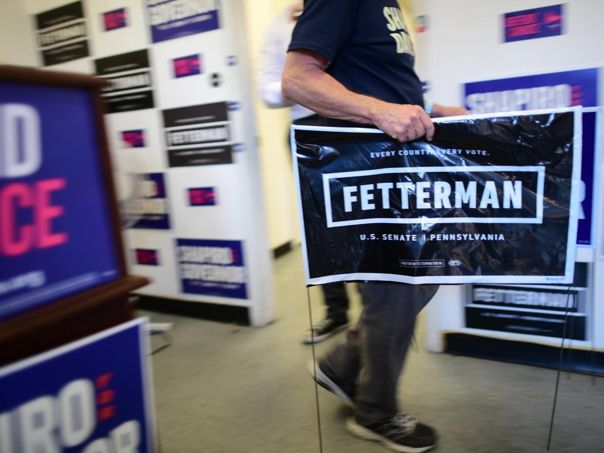 A staff members blurs past carrying a yard placard for Democratic Pennsylvania Senate nominee John Fetterman at a Democrat's campaign office on October 8, 2022 in Philadelphia, Pennsylvania. Democratic candidate for Governor Pennsylvania Attorney General Josh Shapiro addressed supporters outside.