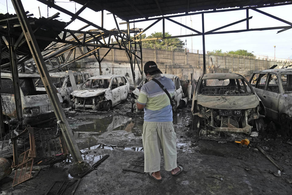 A man stands near burned out vehicles at a neighborhood affected by a fuel depot fire in Jakarta, Indonesia, Saturday, March 4, 2023. A large fire broke out at the fuel storage depot in Indonesia's capital Friday, killing multiple people, injuring dozens of others and forcing the evacuation of thousands of nearby residents after spreading to their neighborhood, officials said. (AP Photo/Tatan Syuflana)