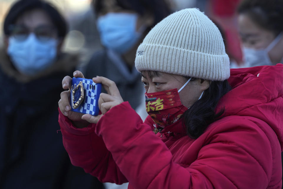 A woman wearing a face mask to help protect from the coronavirus takes a picture on a street in Beijing, Tuesday, Feb. 8, 2022. China has ordered inhabitants of the southern city of Baise to stay home and suspended transportation links amid a surge in COVID-19 cases at least partly linked to the omicron variant. (AP Photo/Andy Wong)