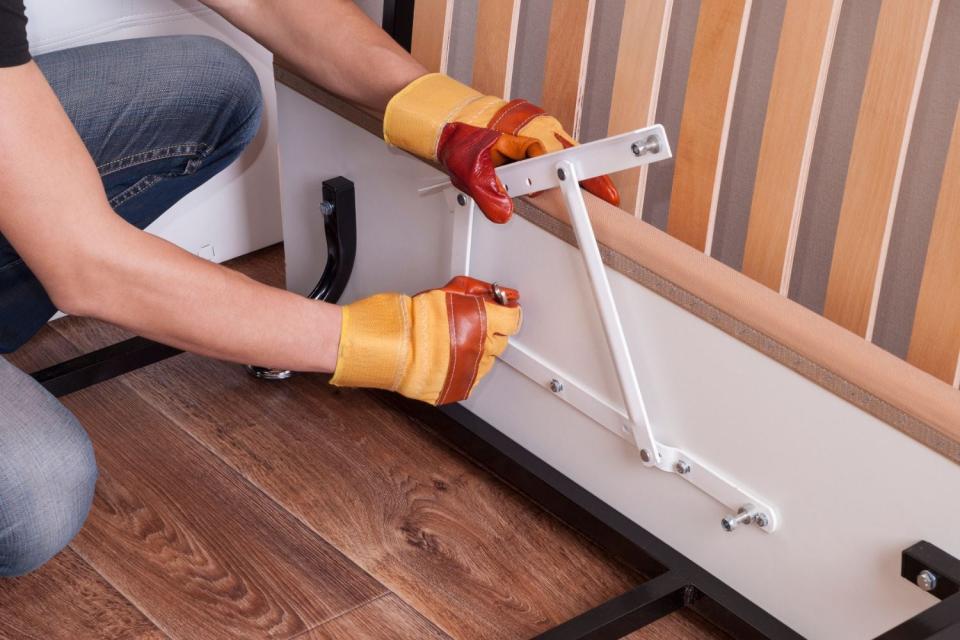 A pair of gloved hands are seen putting a piece of furniture together.