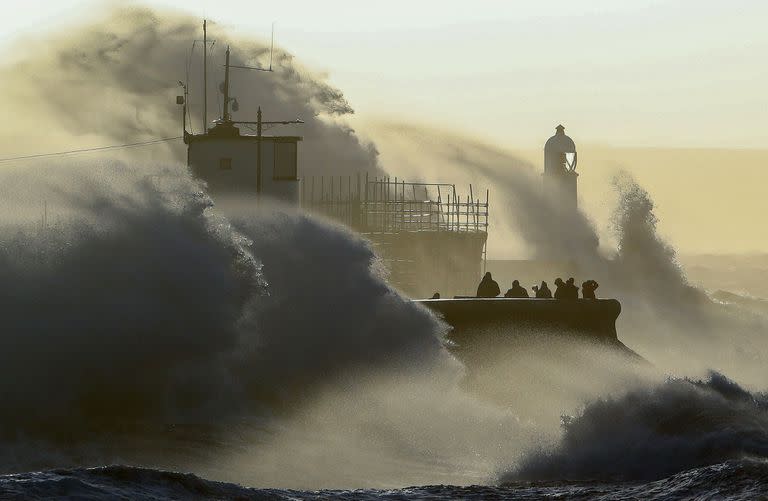 La gente observa cómo las olas chocan contra el muro del mar en Porthcawl, al sur de Gales, el 18 de febrero de 2022 mientras la tormenta Eunice provoca fuertes vientos en toda Gran Bretaña.