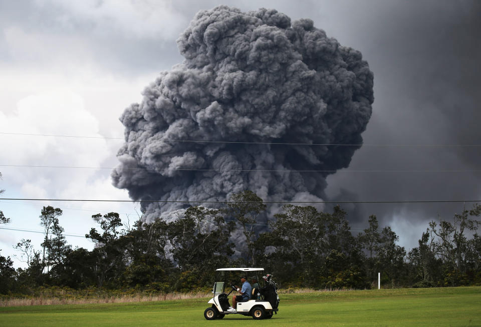 A man drives a golf cart at a golf course as&nbsp;the ash plume rises.