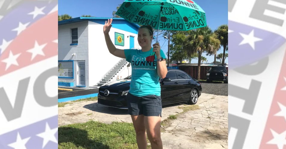Shielded from the sun by a hand-painted umbrella, Julie Shannon, in support of District 2 school board candidate Erin Dunne, waves at motorists across the street from the Dr. Joe Lee Smith Community Center.