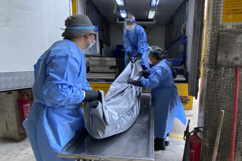 FILE - Workers from the Food and Environmental Hygiene Department, move a corpse from the mortuary to the coffin van at the Queen Elizabeth Hospital in Hong Kong on March 2, 2022. Some hospitals in Hong Kong are currently being overloaded with possible COVID-infected patients. The fast-spreading omicron variant is overwhelming Hong Kong, prompting mass testing, quarantines, supermarket panic-buying and a shortage of hospital beds. Even the morgues are overflowing, forcing authorities to store bodies in refrigerated shipping containers. (AP Photo/Janice Lo, File)