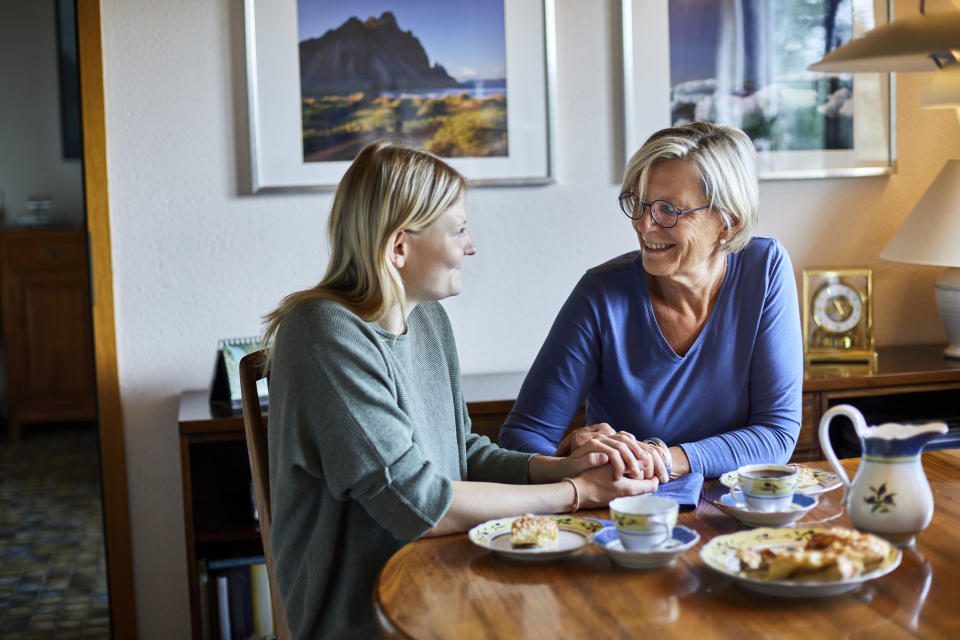 Senior woman and young woman sitting at dining table holding hands (Oliver Rossi / Getty Images)