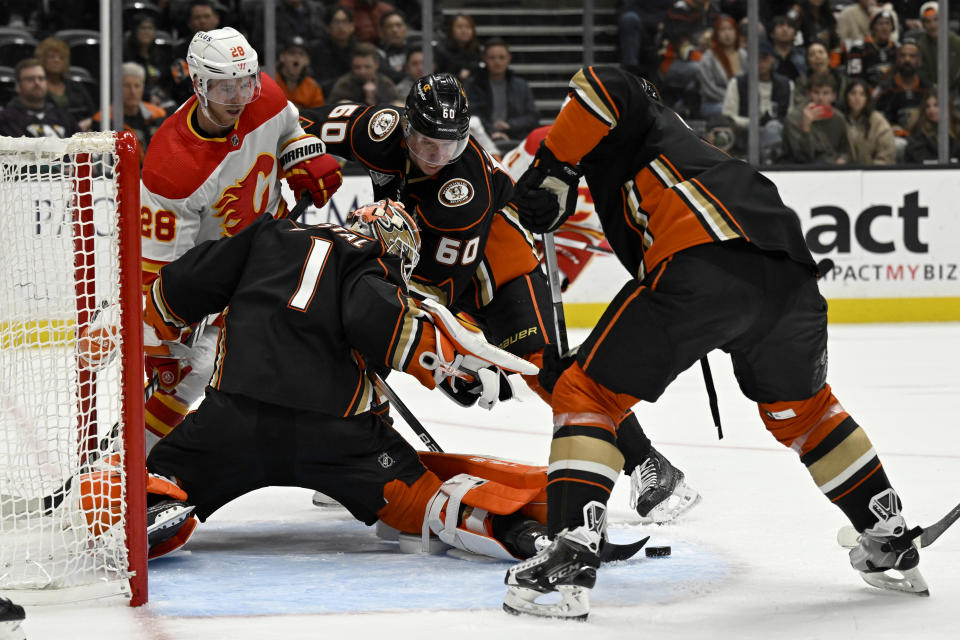 Anaheim Ducks goaltender Lukas Dostal (1) stops a shot with Calgary Flames center Elias Lindholm (28) and defenseman Jackson LaCombe (60) vying for the puck during the second period of an NHL hockey game in Anaheim, Calif., Thursday, Dec. 21, 2023. (AP Photo/Alex Gallardo)