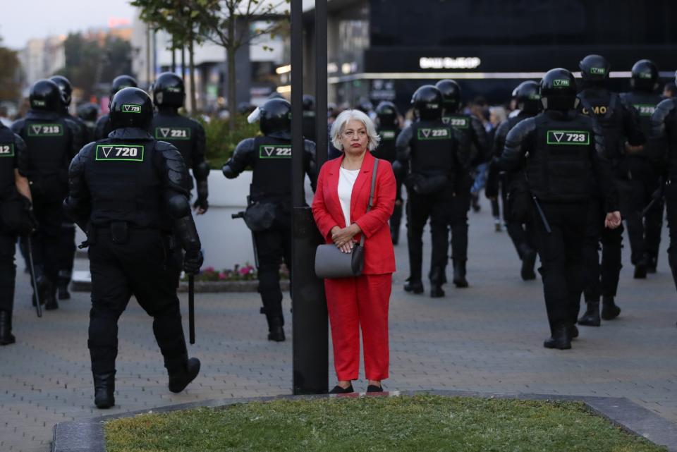 A woman stands in a street as police gather to block protesters during a mass protest following presidential elections in Minsk, Belarus, Monday, Aug. 10, 2020. Thousands of people have protested in Belarus for a second straight night after official results from weekend elections gave an overwhelming victory to authoritarian President Alexander Lukashenko, extending his 26-year rule. A heavy police contingent blocked central squares and avenues, moving quickly to disperse protesters and detained dozens. (AP Photo/Sergei Grits)