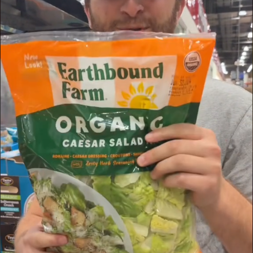 A person in a store holds a bag of Earthbound Farm Organic Caesar Salad Kit