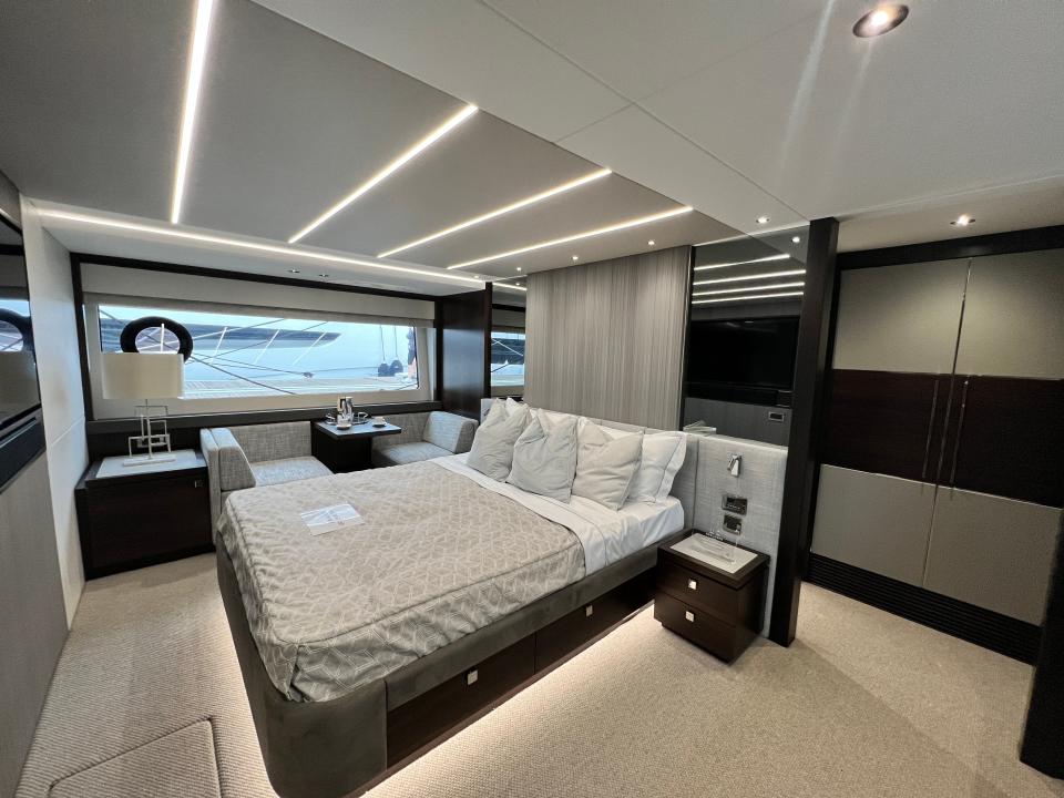 The master cabin of a Sunseeker 76 yacht, grey walls and carpet and linen on the double bed, and grey seats next to a small table.