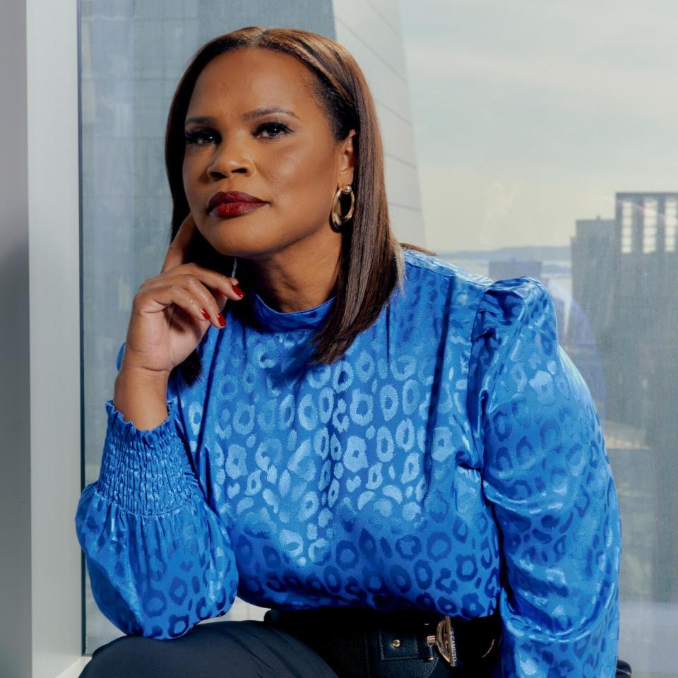 A woman in a blue blouse poses for a portrait looking serious