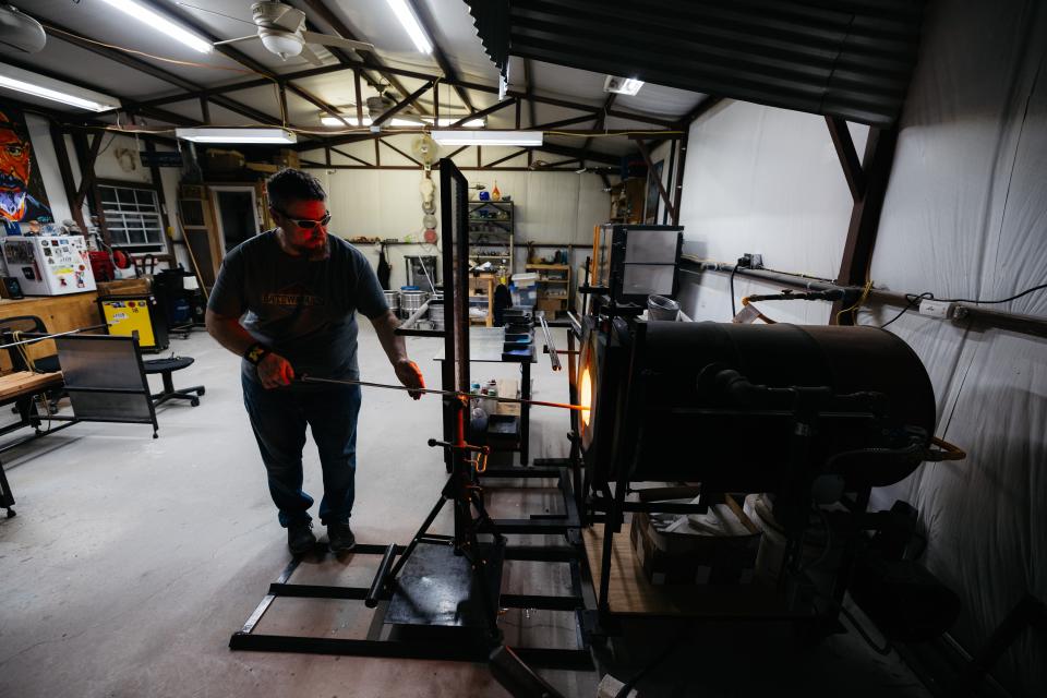 Eric Minton slowly turns the glass egg in the furnace to keep it centered on his pipe.
