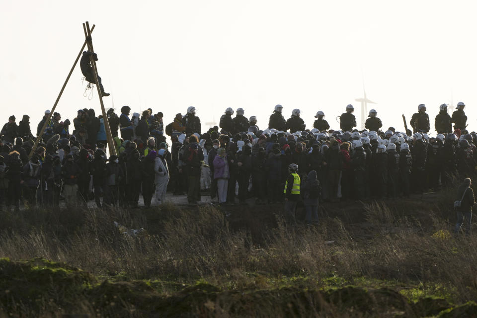 Police officers in riot gear face climate activists at village Luetzerath near Erkelenz, Germany, Tuesday, Jan. 10, 2023. The village of Luetzerath is occupied by climate activists fighting against the demolishing of the village to expand the Garzweiler lignite coal mine near the Dutch border. Poster read: „1,5 degrees celsius means: Luetzerath stays". (AP Photo/Michael Probst)