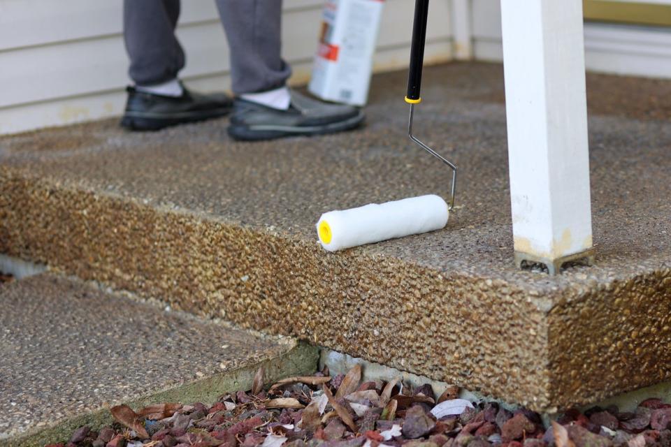 Clear Sealing concrete porch with a paint roller in front of a home