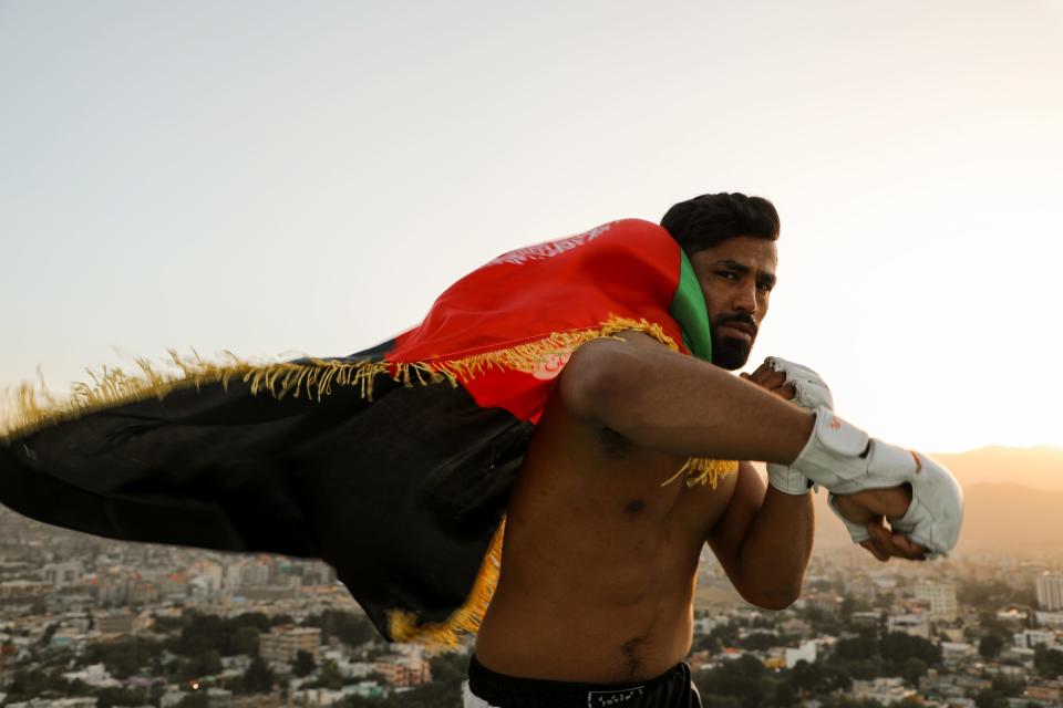 With the skyline in the background, a man, shirtless, wears the Afghan flag as he shadow-boxes.