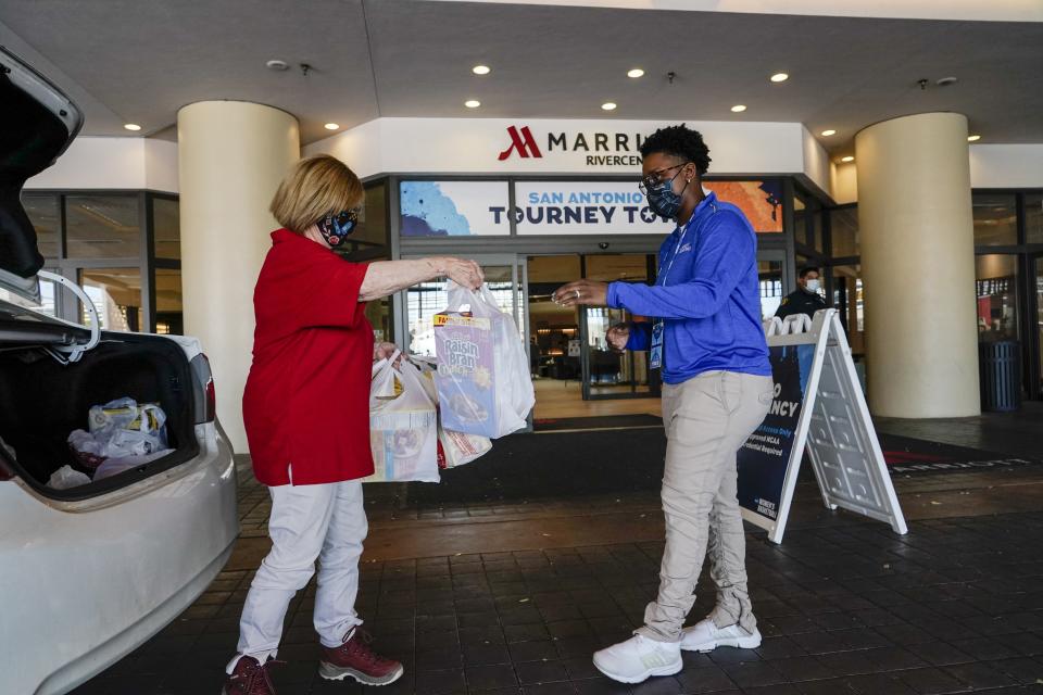 Volunteer Joan Kearl hands food to Amber Wilson outside a hotel Friday, March 26, 2021, in San Antonio. Kearl picked up the food for the quarantined Louisville women's basketball team participating in the NCAA tournament. The NCAA and local organizing groups set up expanded ambassador and item-delivery services relying on volunteer help to take care of needs for players, officials and others working inside. (AP Photo/Morry Gash)