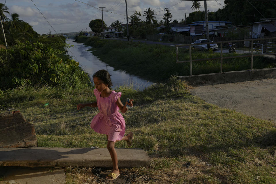 A girl runs next to a gate on the seawall in Tuschen, Guyana, Thursday, April 13, 2023. During the mid-1990s, the Inter-American Development Bank was advising Guyana to relocate communities inland since most of its people live along the coast, and much of its economic activity and agriculture are based there. But people have been reluctant to leave. (AP Photo/Matias Delacroix)