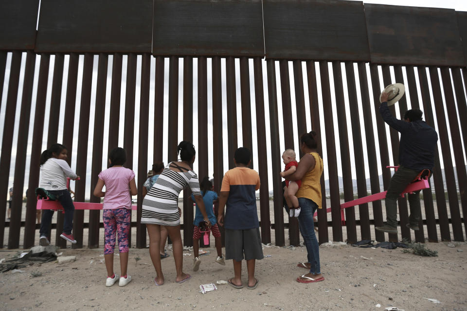 CORRECTS THE FIRST NAME OF THE PROFESSOR TO RONALD, NOT RONALDO AND THE LAST NAME OF THE PHOTOGRAPHER TO CHAVEZ, NOT TORRES - Children and a man play seesaw installed between the border fence that divides Mexico from the United States in Ciudad de Juarez, Mexico, Sunday, July 28, 2019. The seesaw was designed by Ronald Rael, a professor of architecture in California. (AP Photo/Christian Chavez)